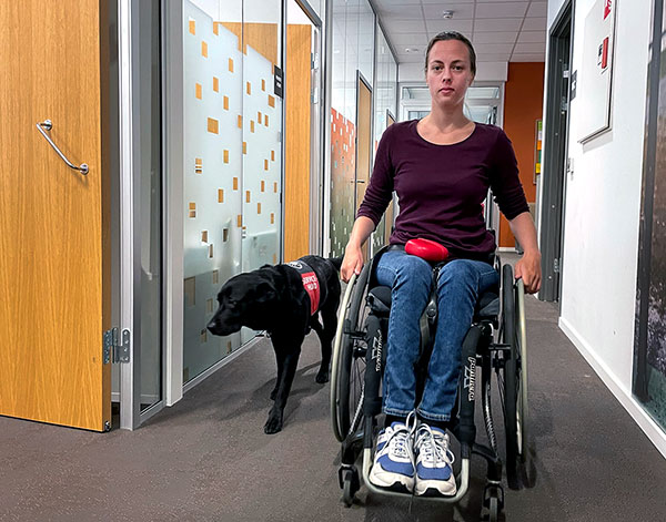 Maren Huseby i rullestol i korridor sammen med servicehund