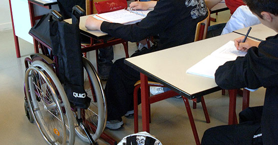 Studenter ved skolepulter, en sammenslått rullestol ved siden av pult