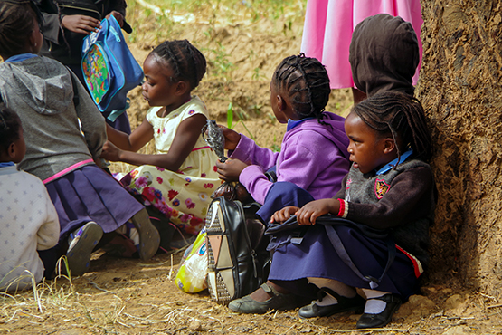 Skolebarn i Zambia sitter ute med skoleransler ved siden av seg