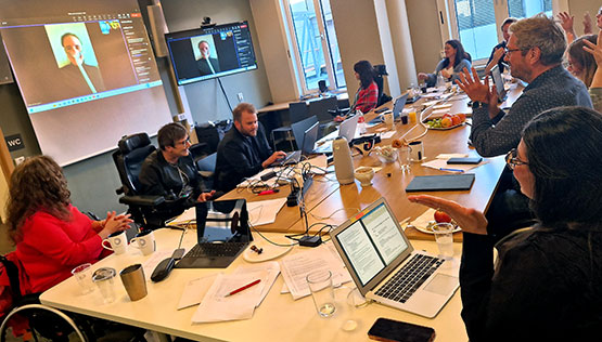 Sentralstyremøtet samlet rundt møtebord, Ingrid Thunem deltar via Teams på storskjerm