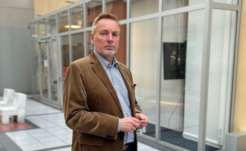 Regionleder Karl Haakon Sævold er avbildet i en korridor. Han har brun dressjakke og lys skjorte, og ser alvorstynget rett i kamera med hendene samlet.