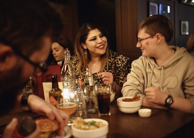 To kvinner ser smilende på hverandre ved restaurantbord sammen med andre venner