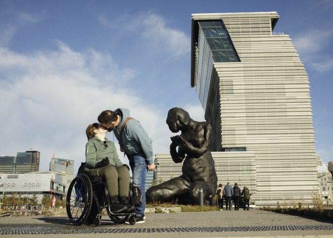 Kvinne i rullestol kysser kjæresten sin foran Munchmuseet