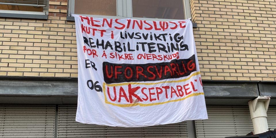 En hjemmelaget banner henger fra et vindu på Aker sykehus. På banneret står at hensynsløse kutt i rehabiliteringen er uforsvarlig.