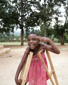 Foto fra TV-aksjonen reise til Uganda. En ung jente med krykker smiler til kamera. 